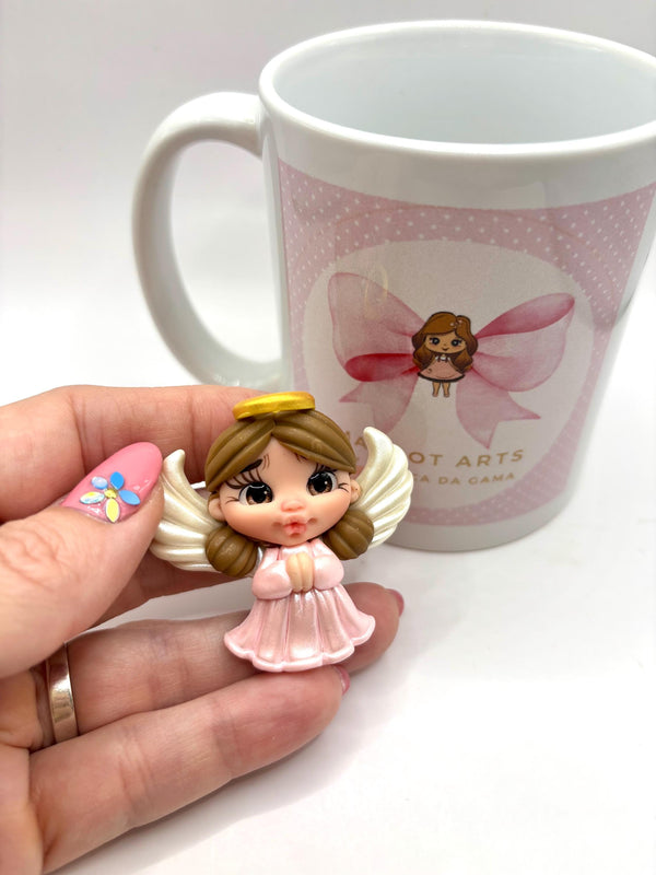Small angel figurine held in a hand with a mug featuring a cartoon character in the background.