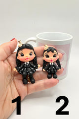 Two black hair figurines held in a hand with a white mug in the background